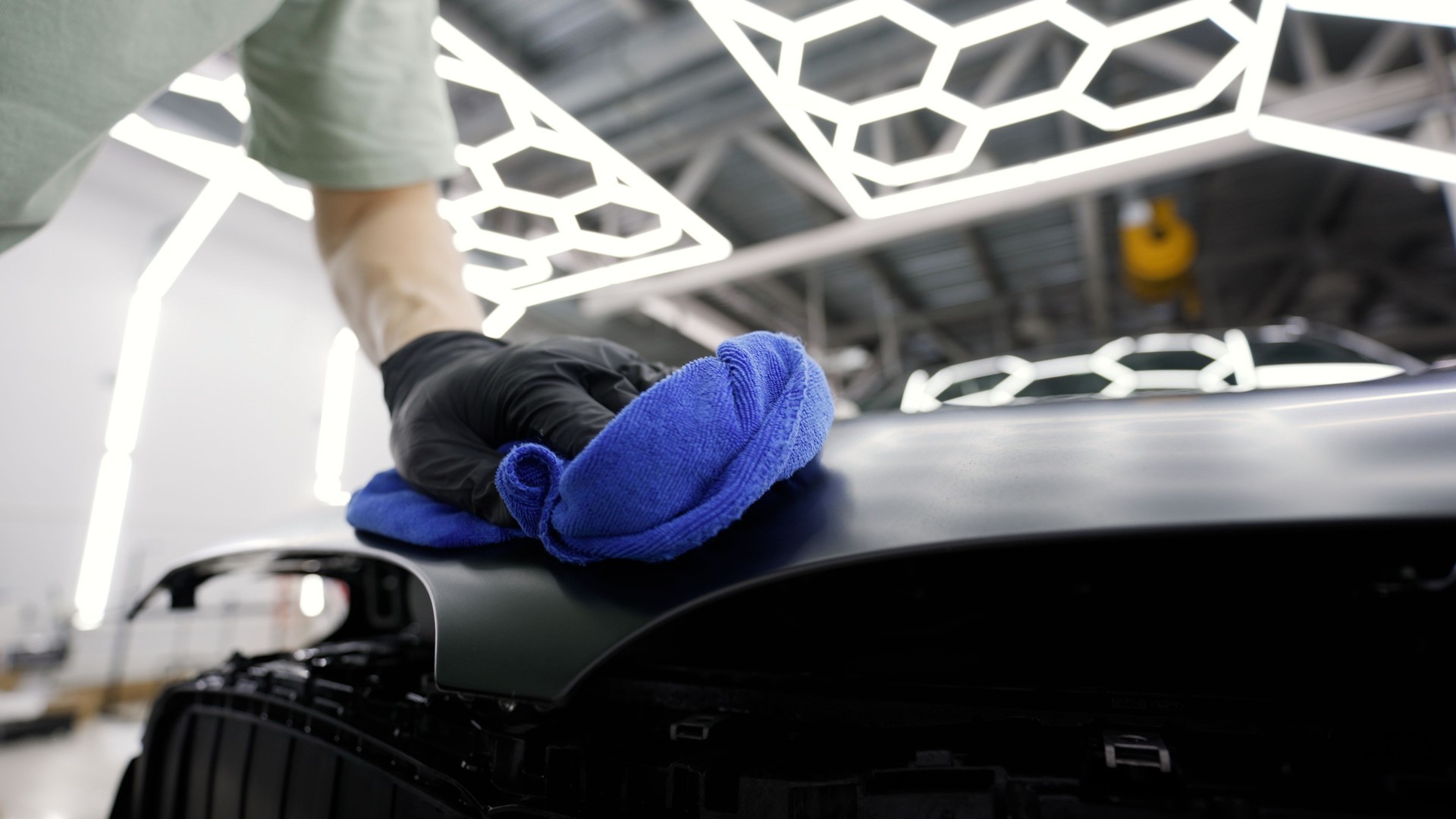 Car detailer polishing hood of vehicle in auto shop